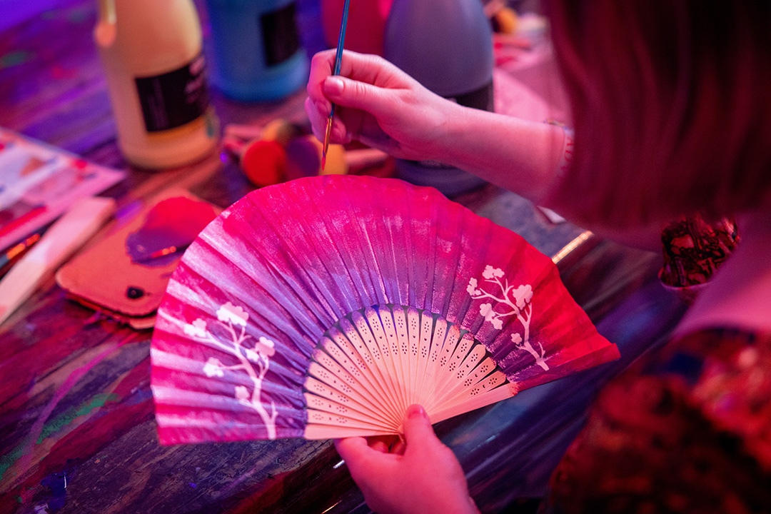 A close up of a Fan Festival 2026 in Berlin attendee painting a paper fan.