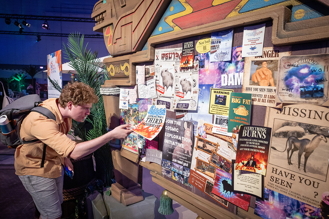 A Fan Festival 2026 in Berlin attendee inspecting a market board filled with colourful Final Fantasy 14-themed advertisements and posters.