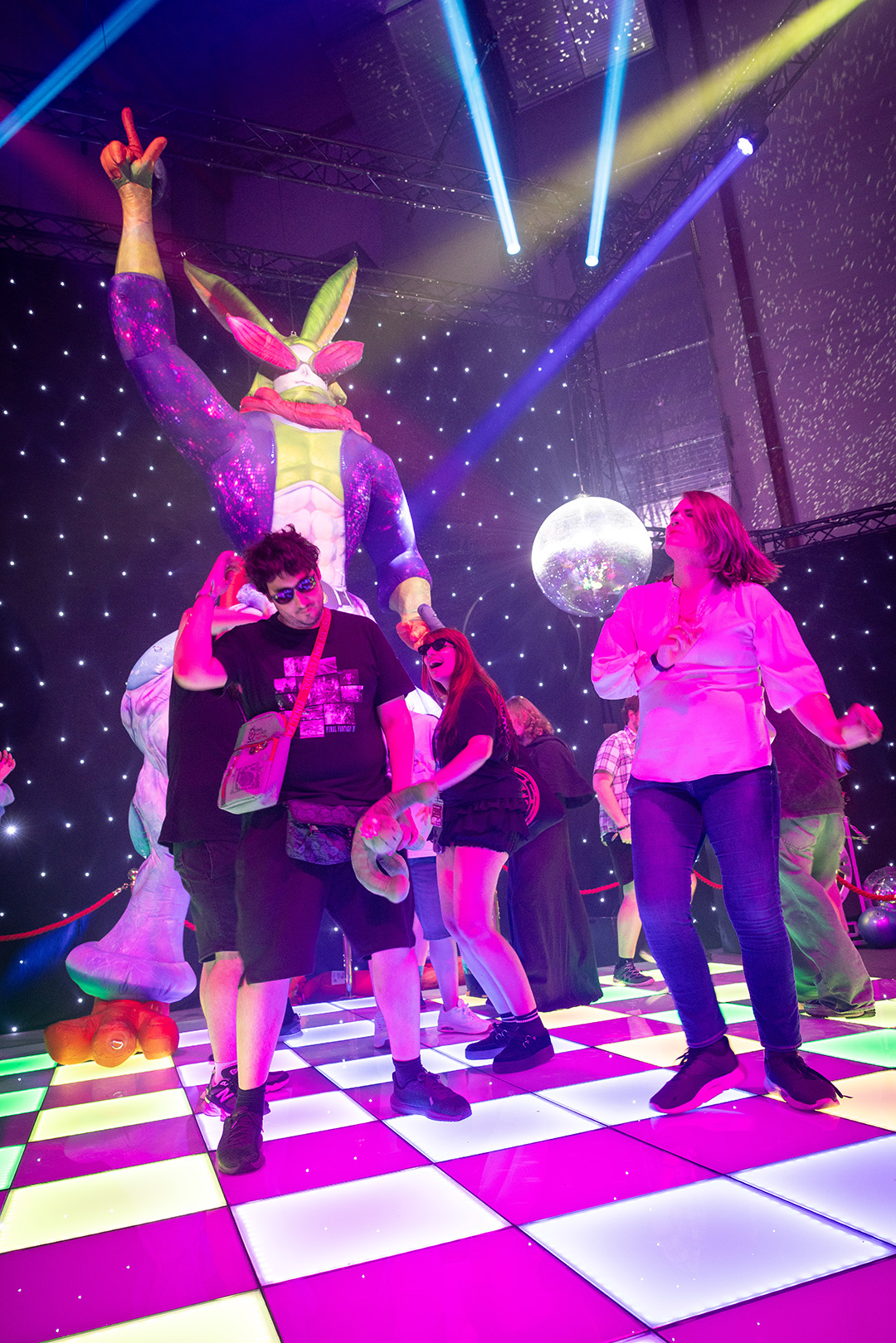A photograph of Fan Festival 2026 in Berlin attendees dancing on a colourful dance floor with a large inflatable Dancing Green character posing behind them.