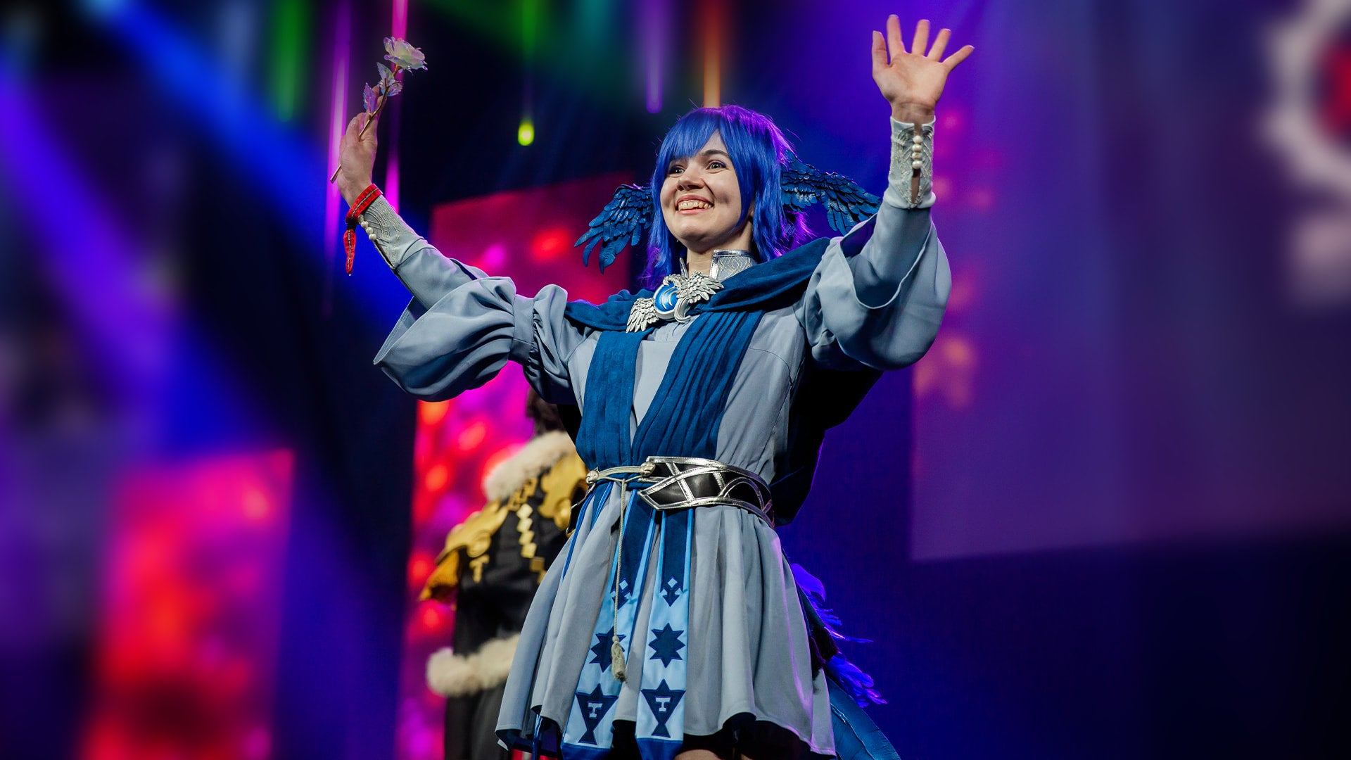 A cosplayer dressed as Meteion from Final Fantasy 14 with her hands up waving to the crowd on the Fan Festival 2023 in Las Vegas event stage